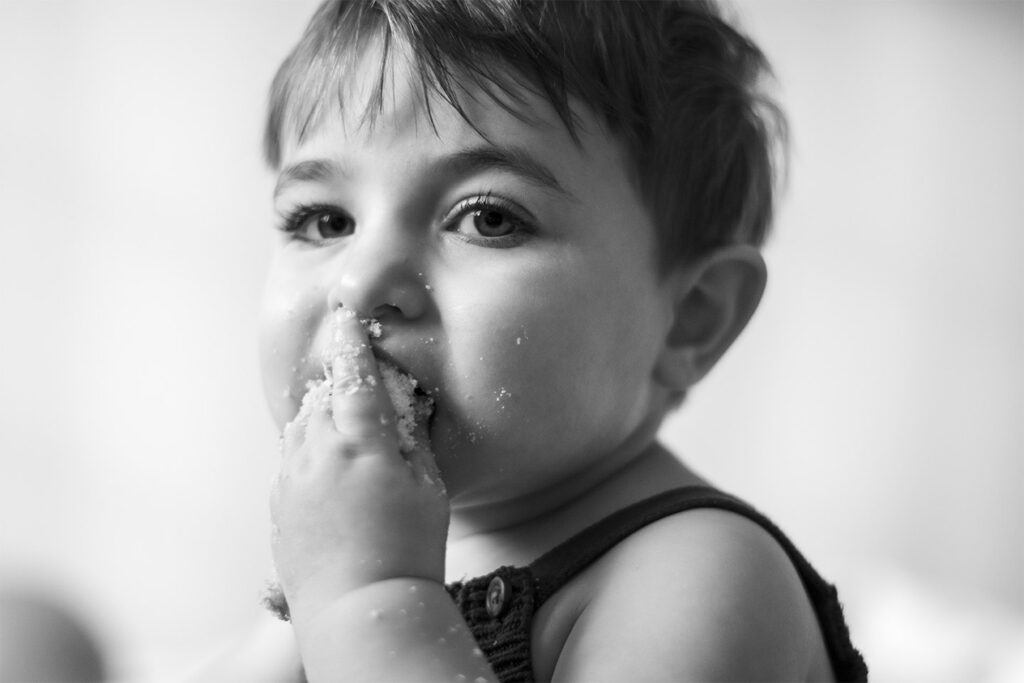 Black and white image of little boy eating cake
