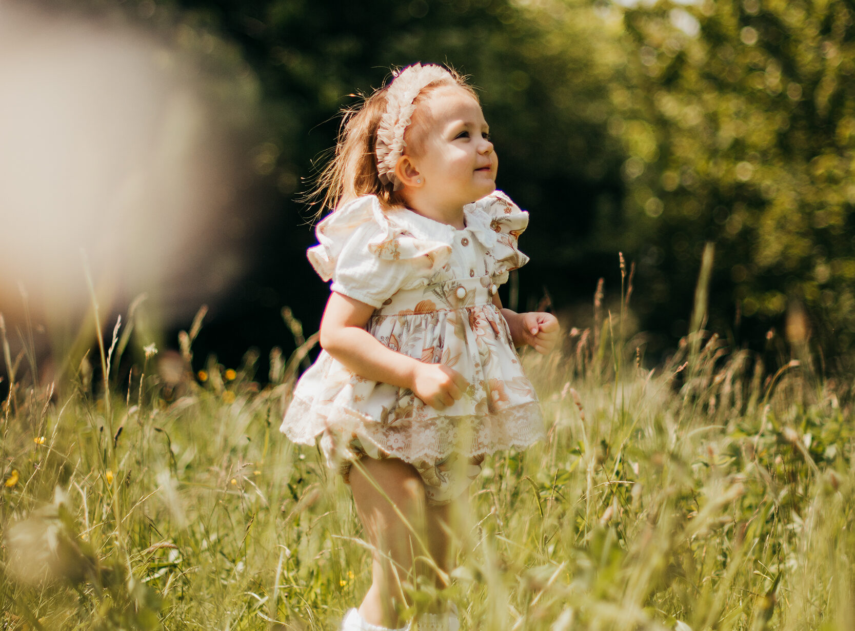Image of little girl wearing a vintage dress in a green long grass field. 